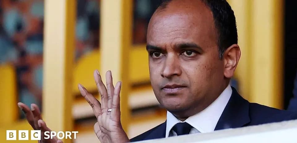 Person gesturing from a VIP box at a stadium