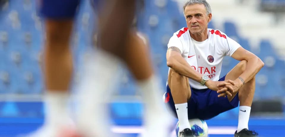 Coach squatting on training pitch observing players