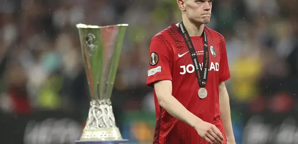 Player in red jersey walking past trophy with medal