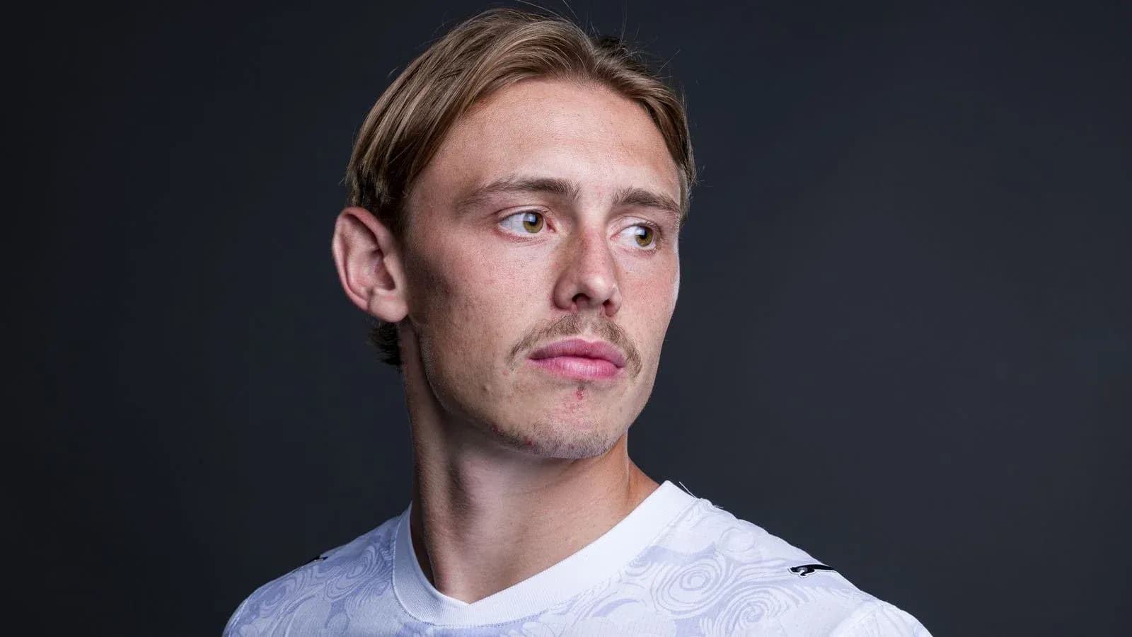 Player posing in white jersey against dark background