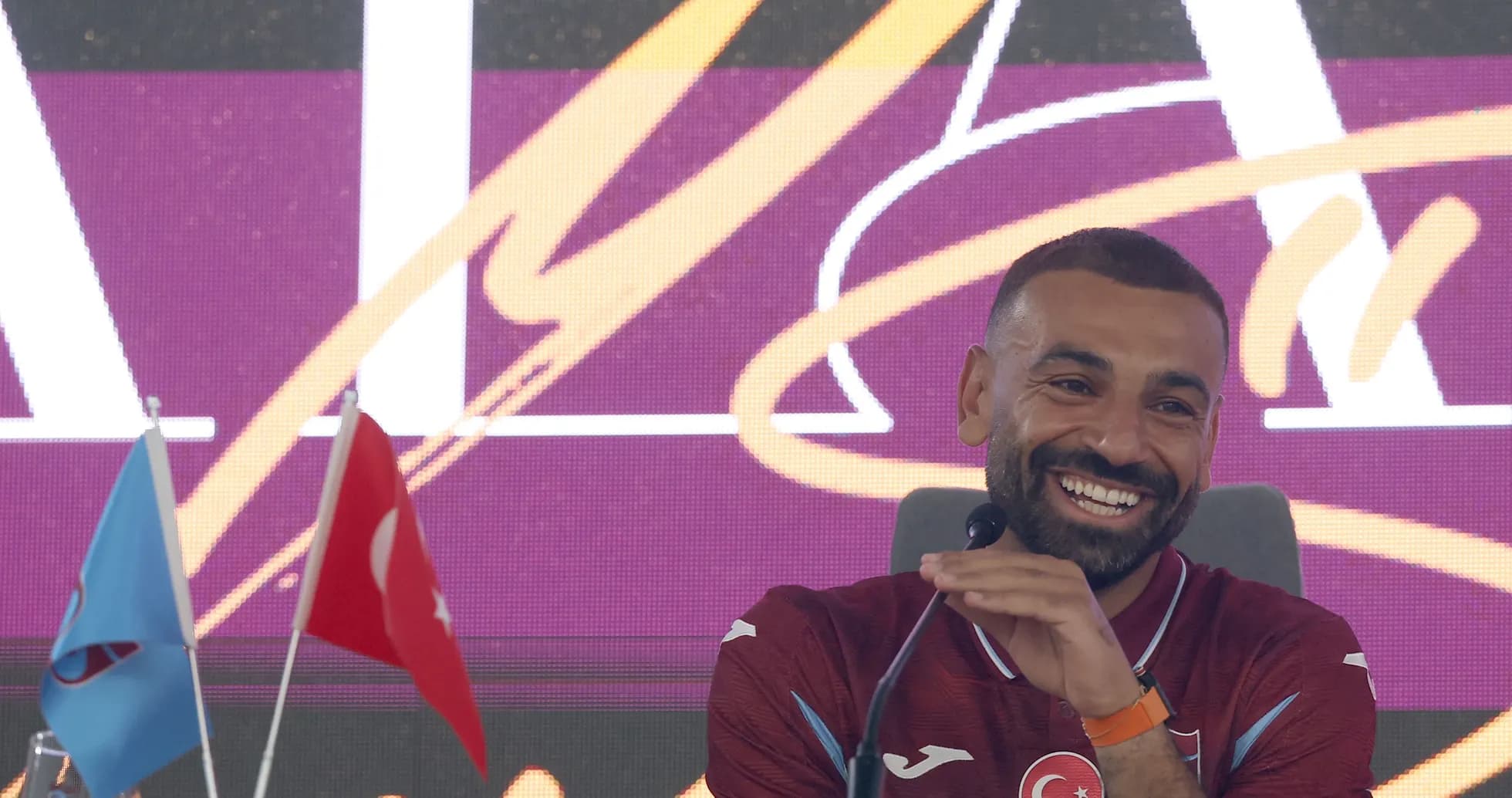 Player smiling at press conference with flags