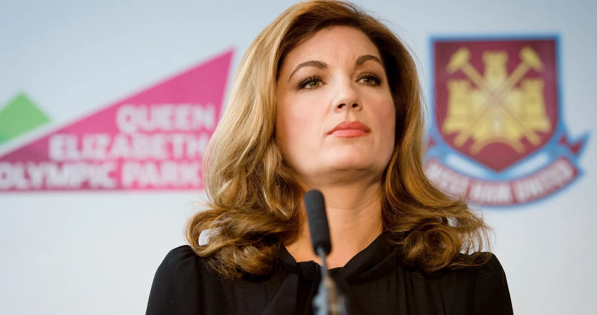 Woman speaking at press conference with team logo