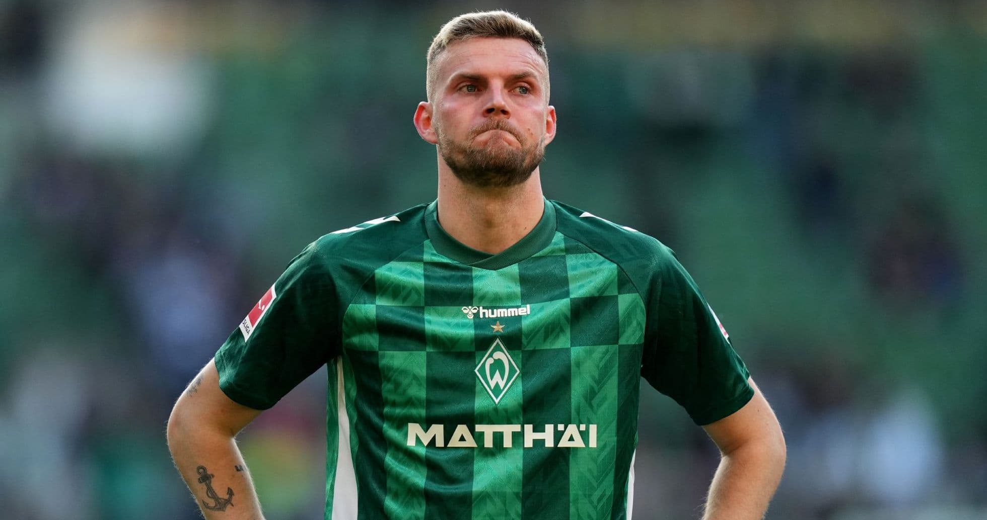 Player in green jersey stands with serious expression