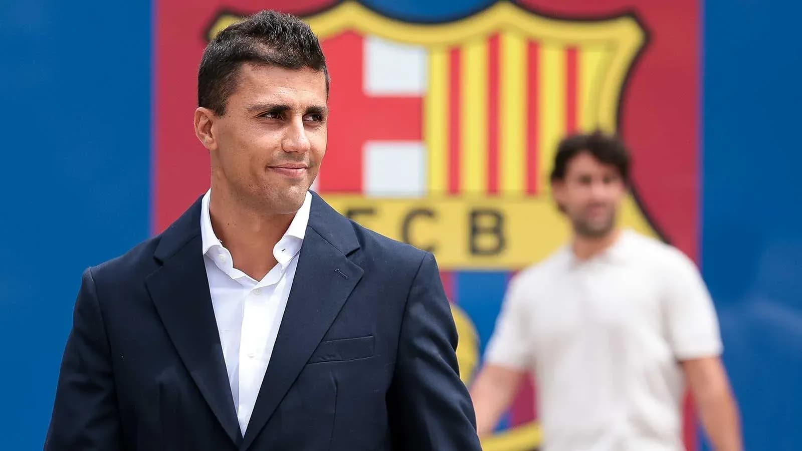 Man in suit standing in front of Barcelona logo Man in suit standing in front of Barcelona logo