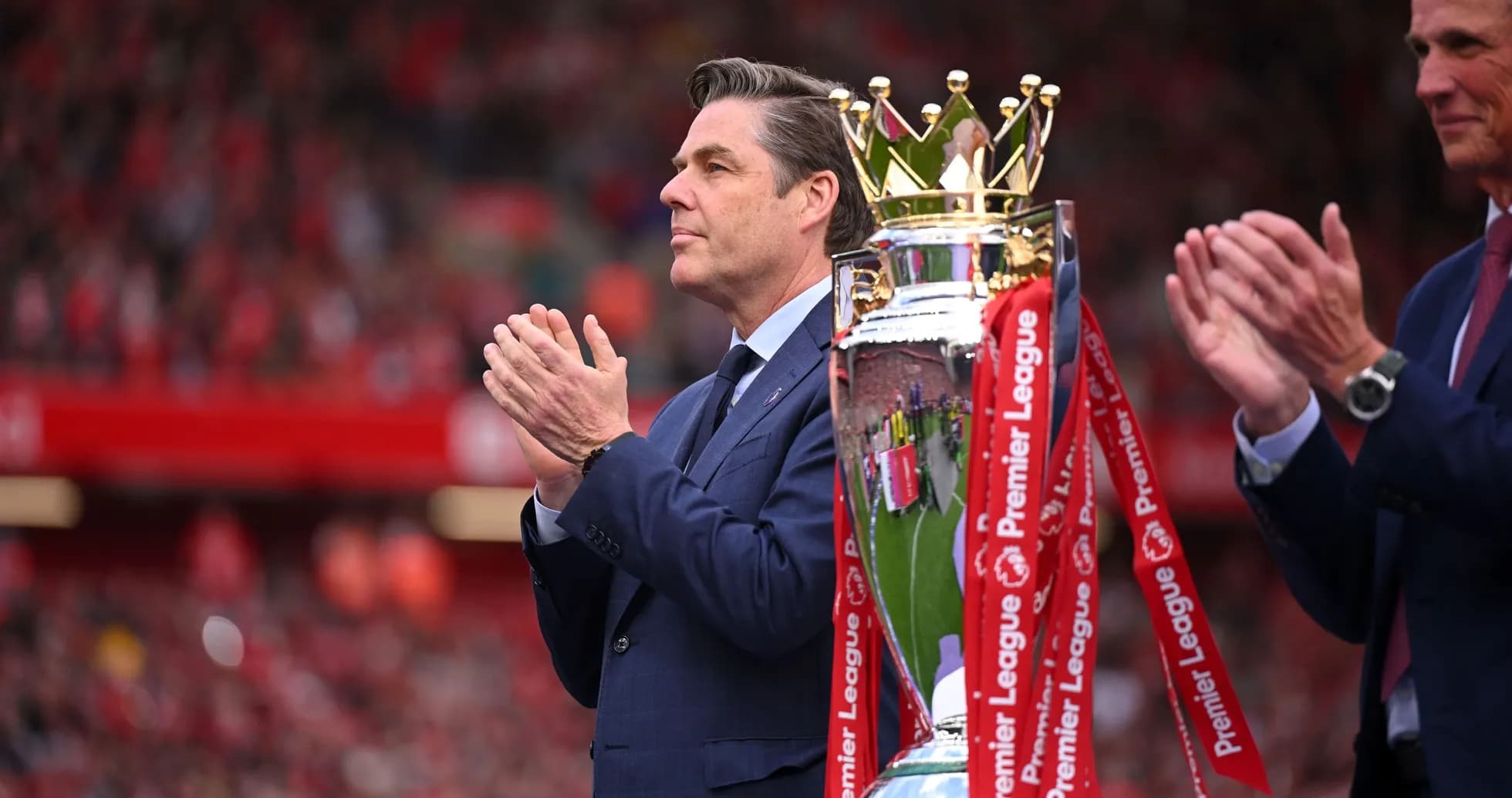 Man applauding next to the Premier League trophy