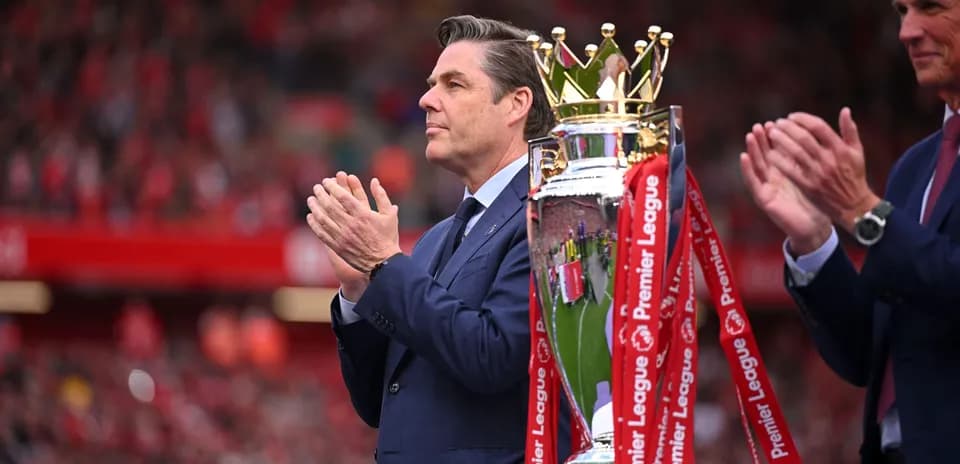 Man applauding next to the Premier League trophy