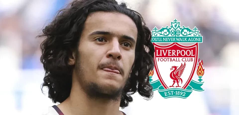 Player with curly hair in front of Liverpool logo