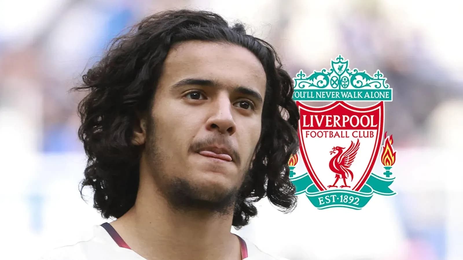 Player with curly hair in front of Liverpool logo