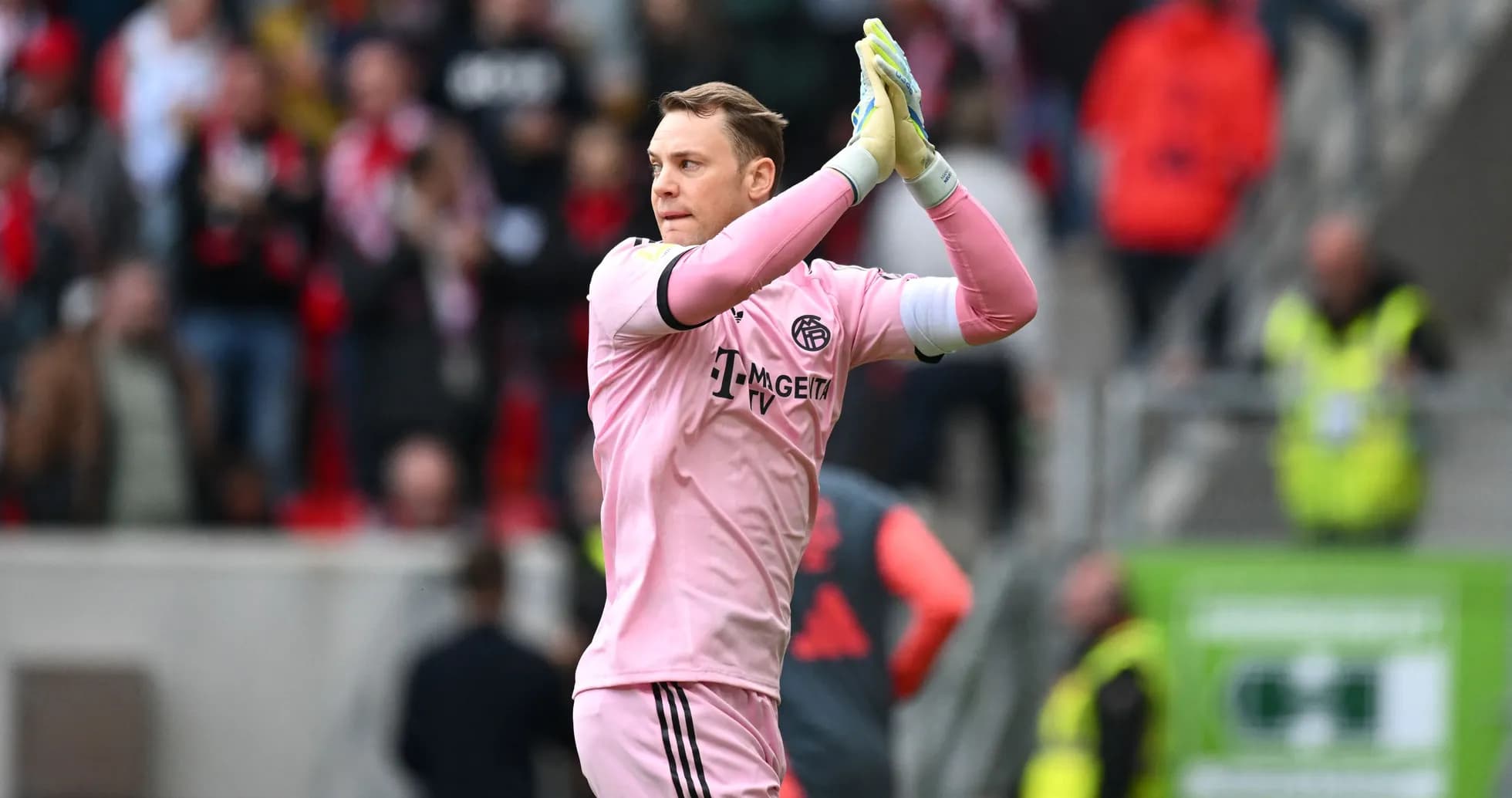 Goalkeeper in pink kit applauding fans after match