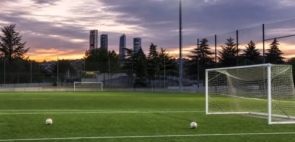 Football pitch with goal and city skyline at sunset