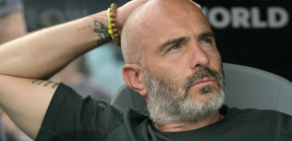 Coach seated, hand on head during match