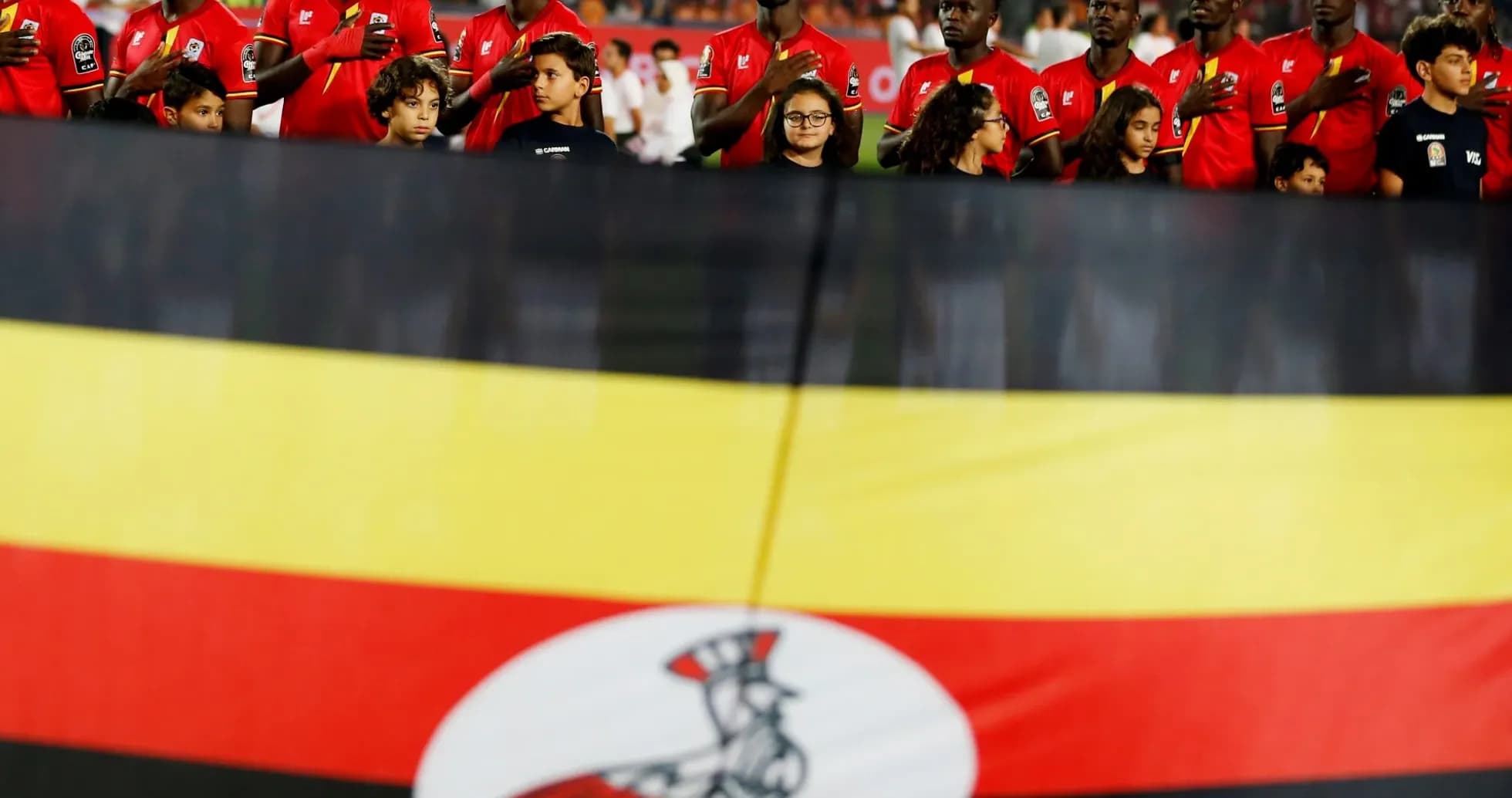 Ugandan players singing national anthem with flag