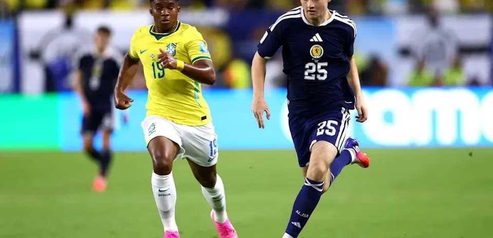 Player from Scotland dribbling the ball, Brazilian defender pursuing