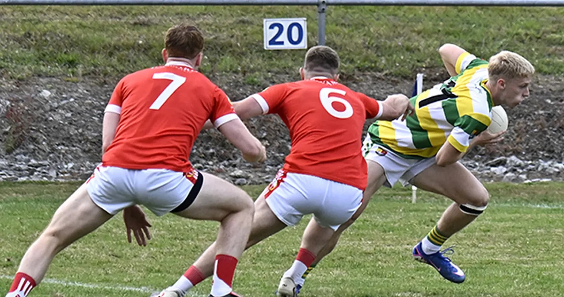 Player in green shirt evading two defenders in red