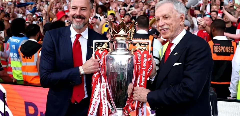 Two officials holding Premier League trophy with crowd celebrating