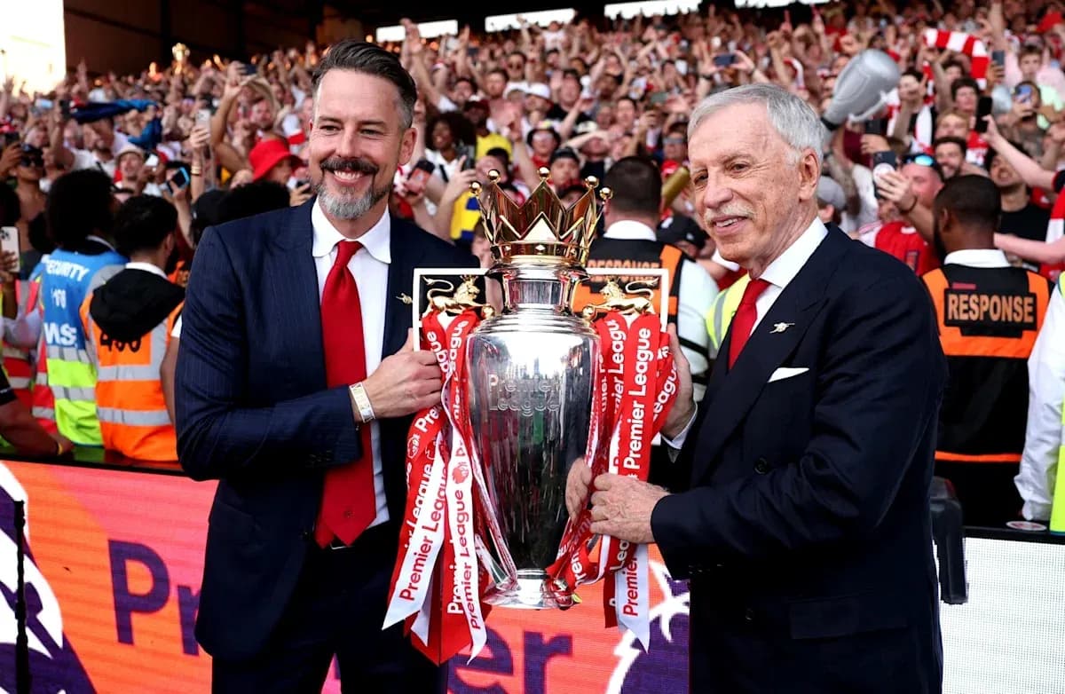Two officials holding Premier League trophy with crowd celebrating
