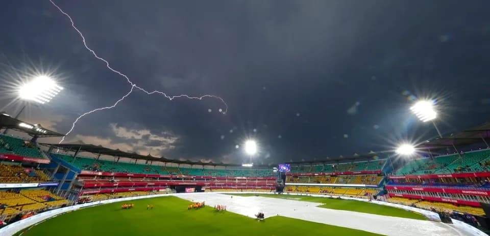 Lightning strikes over a cricket stadium with covers