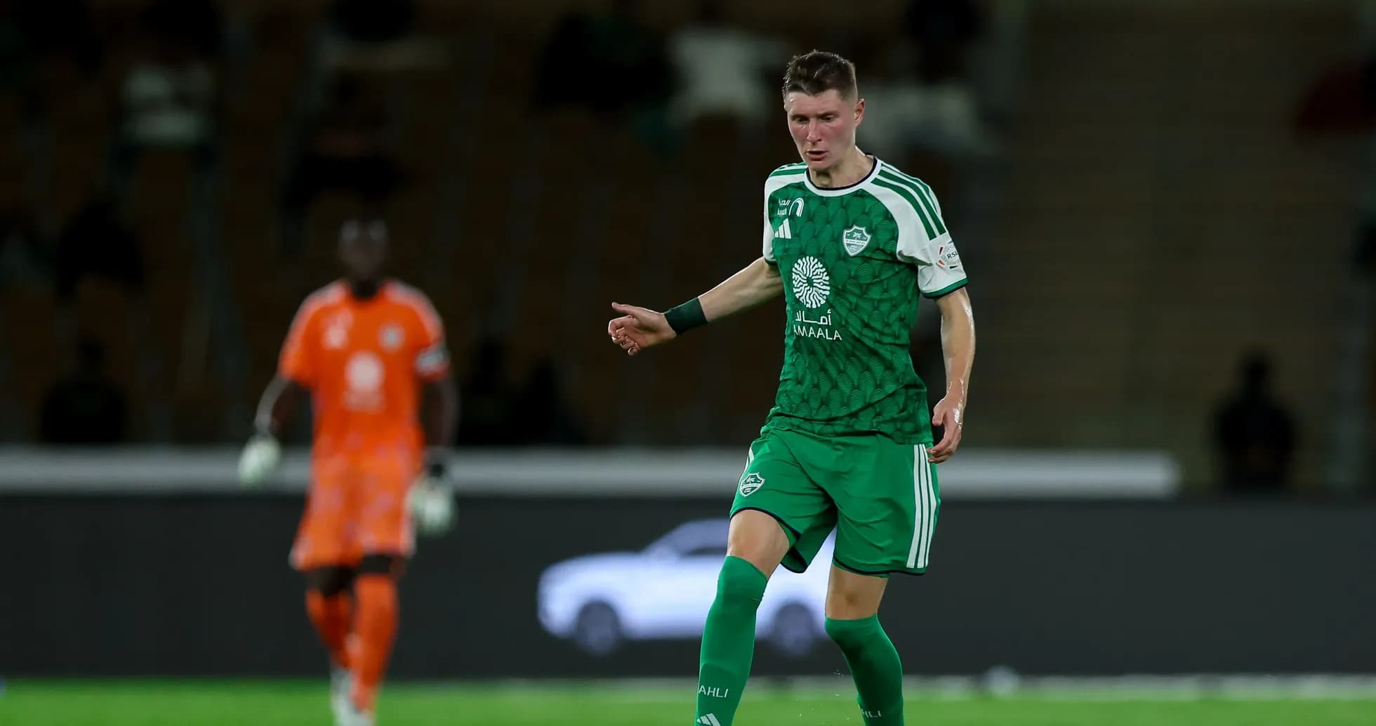 Player in green kit dribbling ball on field