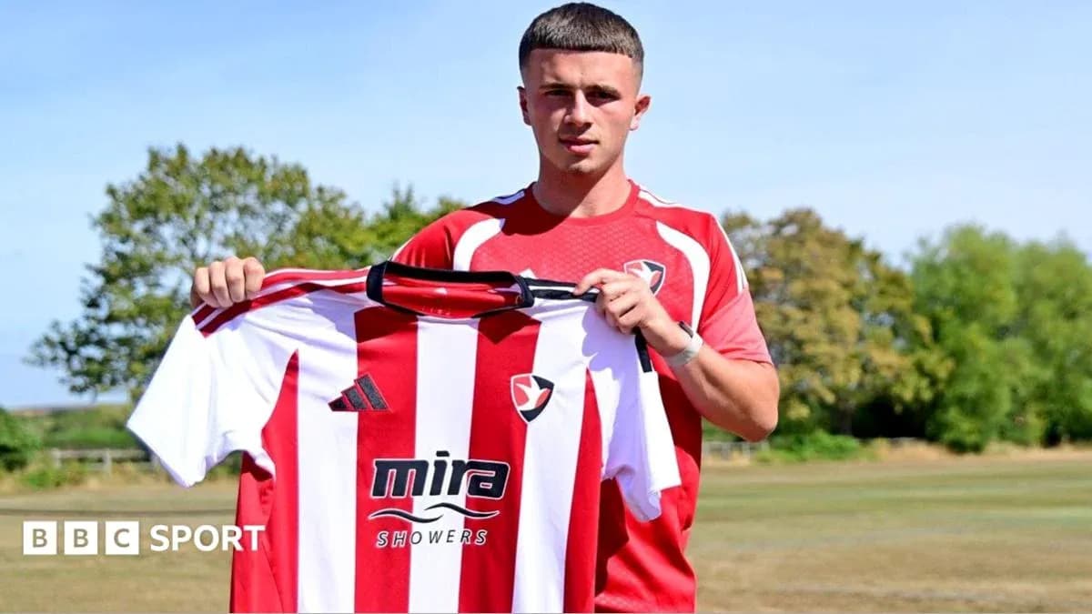 Player holding Cheltenham Town jersey during signing event Player holding Cheltenham Town jersey during signing event