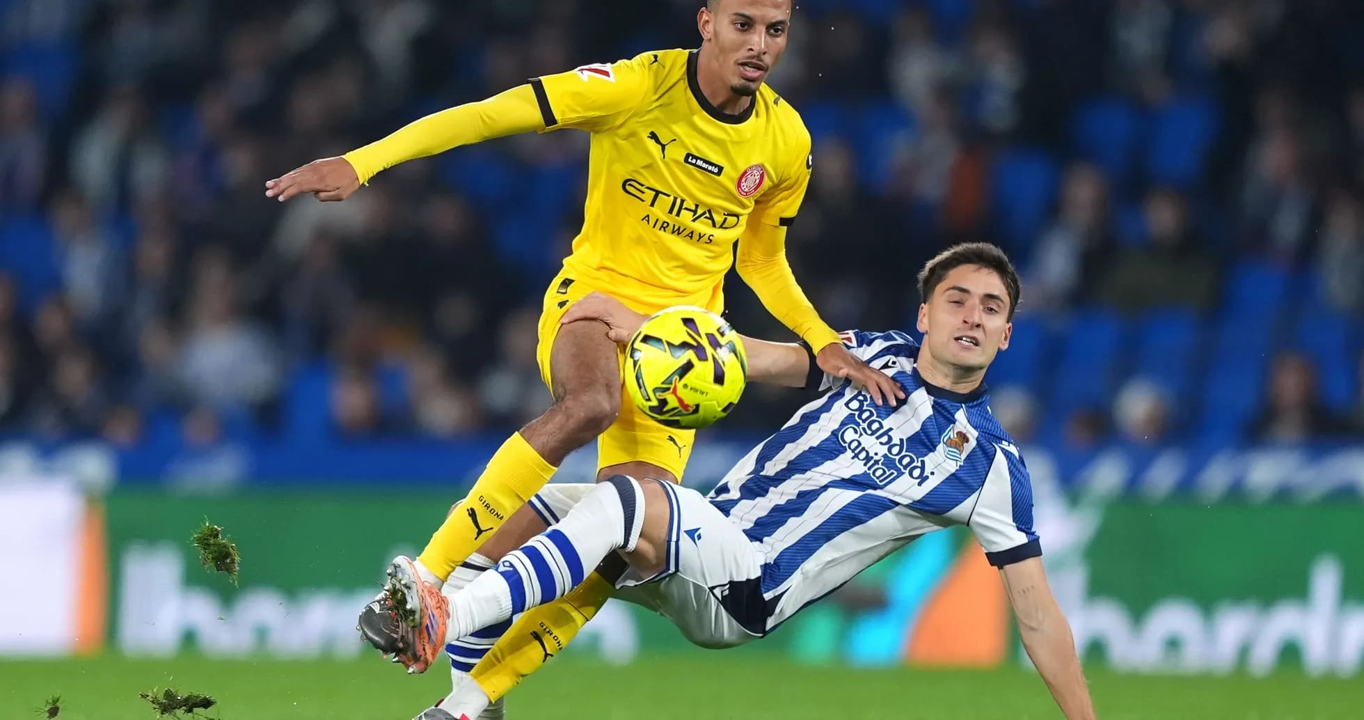Girona player challenging Real Sociedad opponent Girona player challenging Real Sociedad opponent