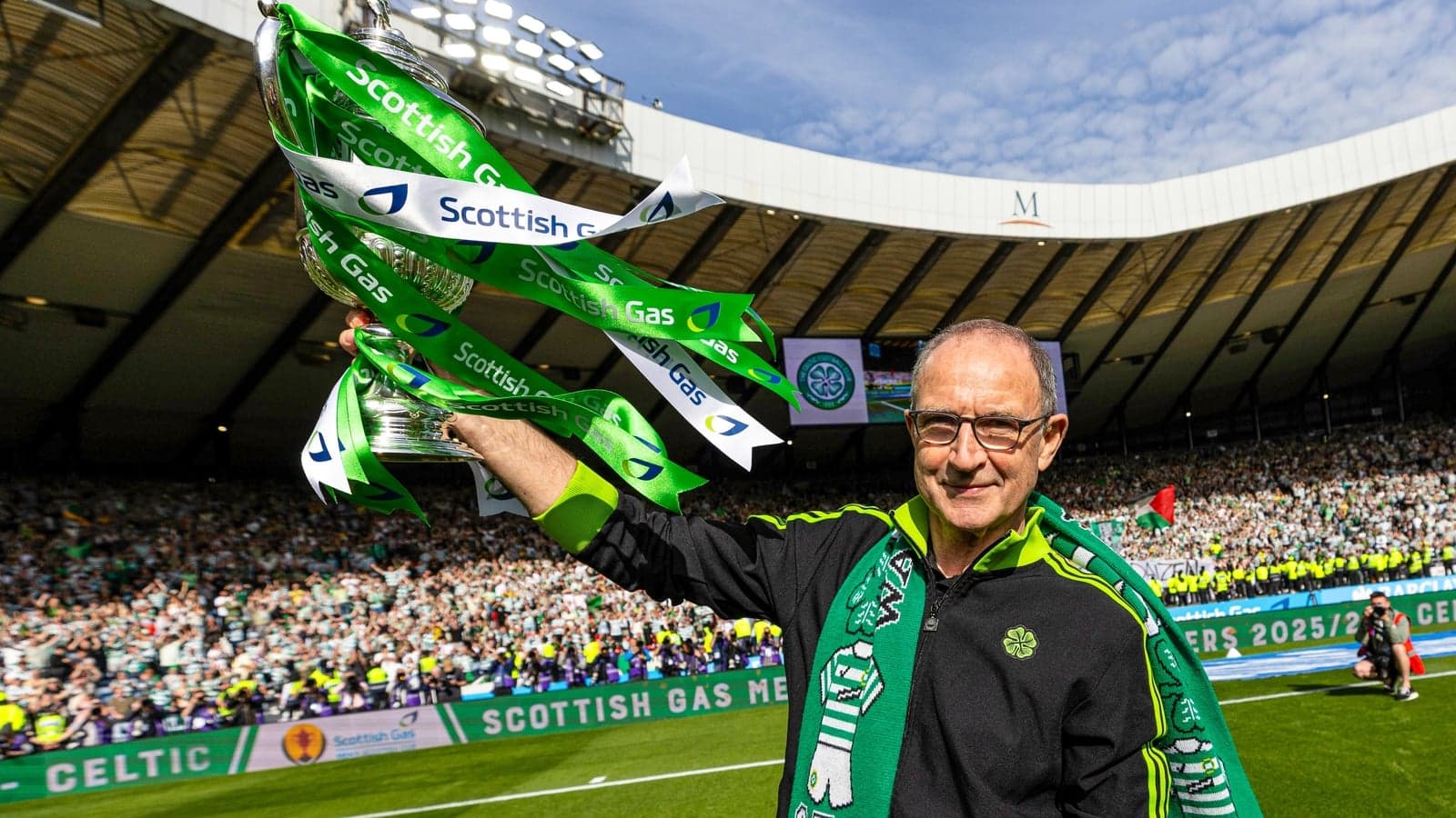 Man holding trophy with Celtic fans celebrating in background Man holding trophy with Celtic fans celebrating in background